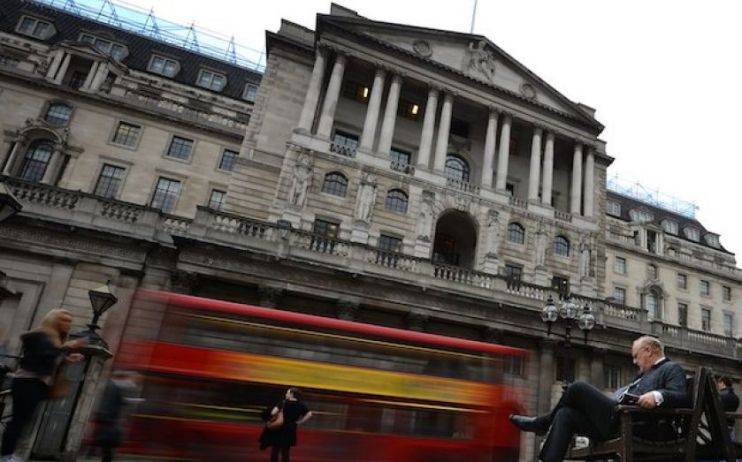 A red London bus passes in front of the Bank of England