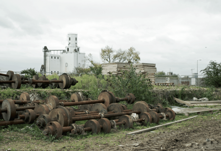 Derelict Millennium Mills in Royal Docks, London, with rusty industrial equipment in the foreground.