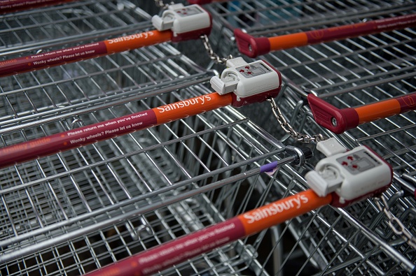 The logos of supermarket chain Sainsbury's are pictured on the handles of shopping trolleys outside a store in Stockport, northern England on April 30, 2018. - Britain's second and third biggest supermarket chains Sainsbury's and Walmart-owned Asda have agreed to merge, the pair said Monday, hoping to create a &pound;13-billion ($18-billion, 15-billion-euro) retail king and leapfrog UK number one Tesco. The blockbuster deal -- which is effectively a takeover bid with Sainsbury's acquiring a majority 58-percent stake -- comes as the British supermarket sector faces squeezed profit margins and fierce competition from German-owned discounters Aldi and Lidl and online US titan Amazon. (Photo by OLI SCARFF / AFP) (Photo credit should read OLI SCARFF/AFP/Getty Images)