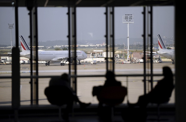 Travellers wait in a lounge at Orly airport, south of Paris, as an Air France's airbus A321 plane is seen parked on the tarmac, on the eight day of the French company Air France pilots' strike. Air France has suspended until December its plans to expand its low-cost subsidiary, unions said on September 22, in a bid to end the longest strike at the airline since 1998. The airline's boss Alexandre de Juniac made the proposal to the unions on September 22, after a week of strike action that has cost the company up to 15 million euros ($19 million) per day. AFP PHOTO / STEPHANE DE SAKUTIN (Photo credit should read STEPHANE DE SAKUTIN/AFP/Getty Images)