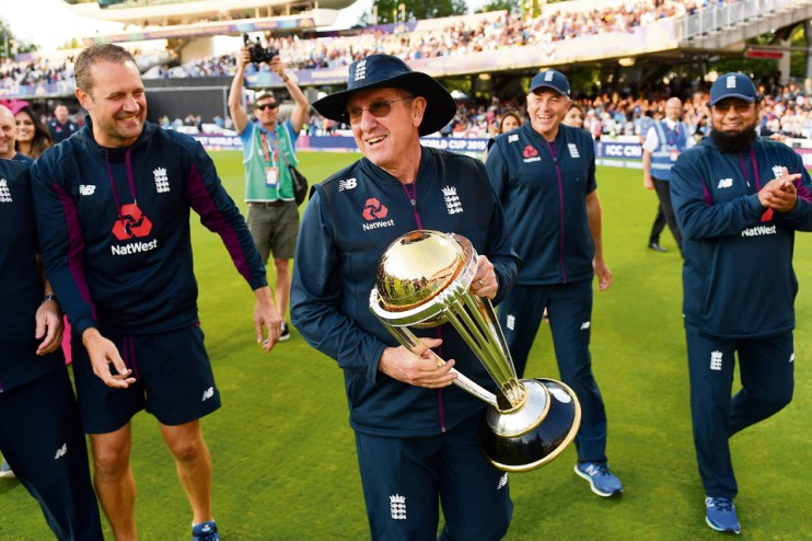 LONDON, ENGLAND - JULY 14: England coach Trevor Bayliss celebrates with the trophy after winning the Final of the ICC Cricket World Cup 2019 between New Zealand and England at Lord's Cricket Ground on July 14, 2019 in London, England. (Photo by Gareth Copley-IDI/IDI via Getty Images)