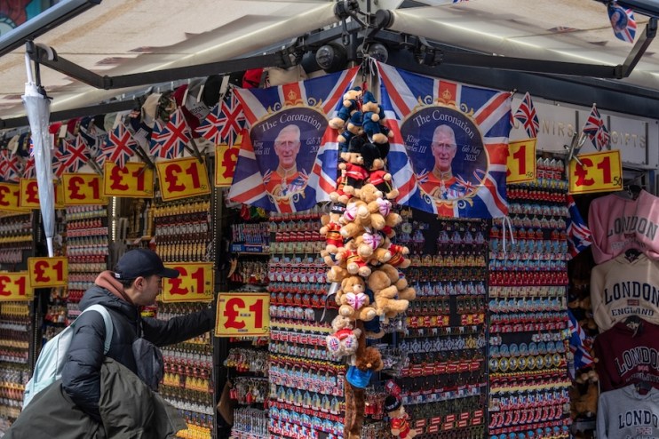 LONDON, ENGLAND - APRIL 24: A man looks at items on display at a souvenir stand as King Charles III Coronation flags are displayed above him on April 24, 2023 in London, England. The Coronation of King Charles III and The Queen Consort will take place on May 6, part of a three-day celebration. (Photo by Carl Court/Getty Images)