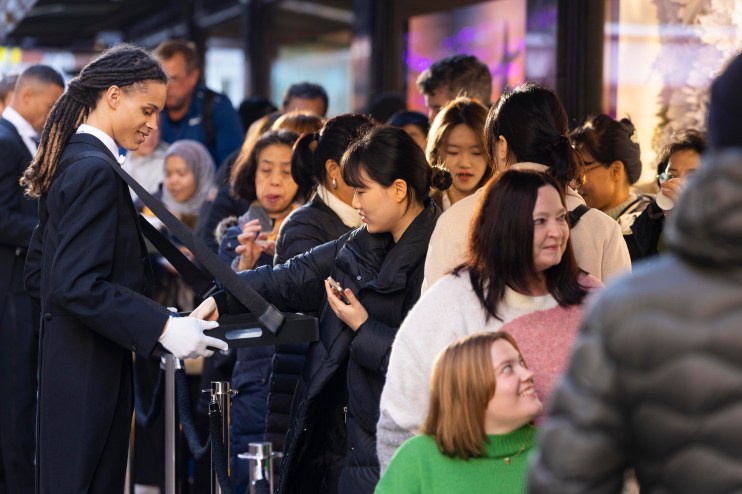 Employees offer refreshments to customers queueing outside Harrods in Knightsbridge, London, in preparation for the launch of its Boxing Day Winter Sale.