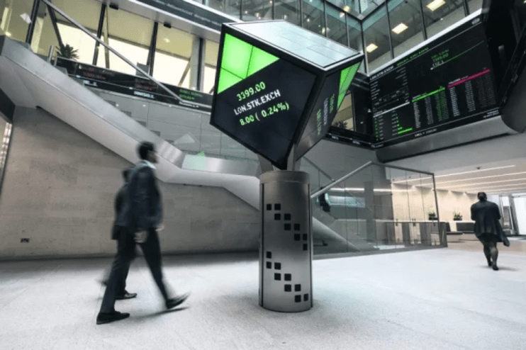 London Stock Exchange interior with a digital display showing LON.STK.EXCH and traders walking past.