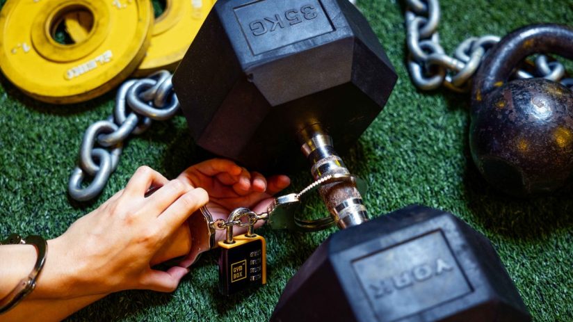 Gymgoer handcuffed to weights symbolizing commitment and investment in fitness stocks amidst 2025 market boom