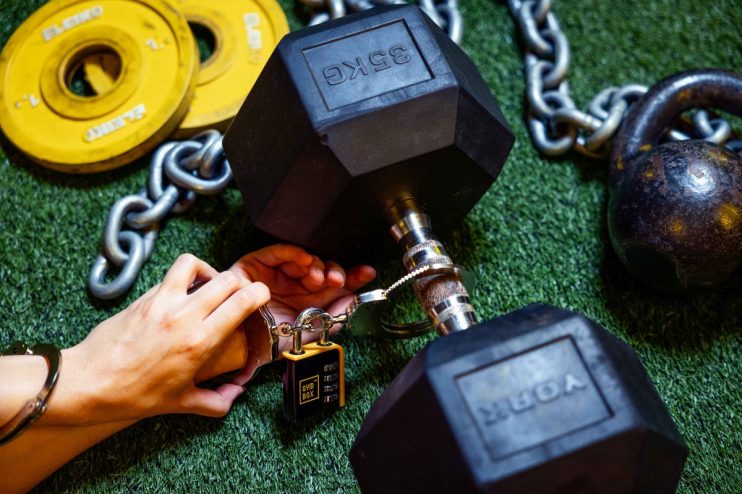 Gymgoer handcuffed to weights symbolizing commitment and investment in fitness stocks amidst 2025 market boom