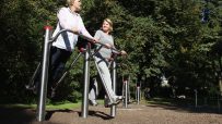 Two older women exercising at an outdoor gym in sunshine