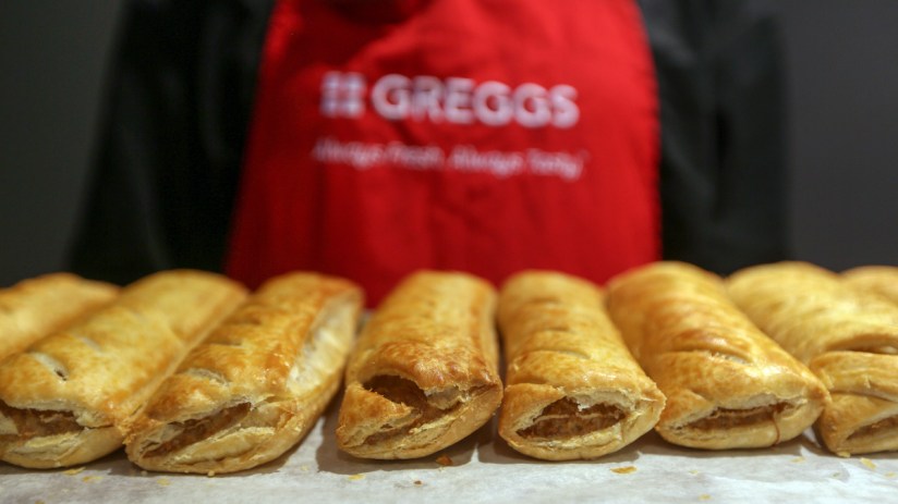 Greggs storefront with customers, highlighting challenges amid a 7.4% sales rise and economic impact on shares.