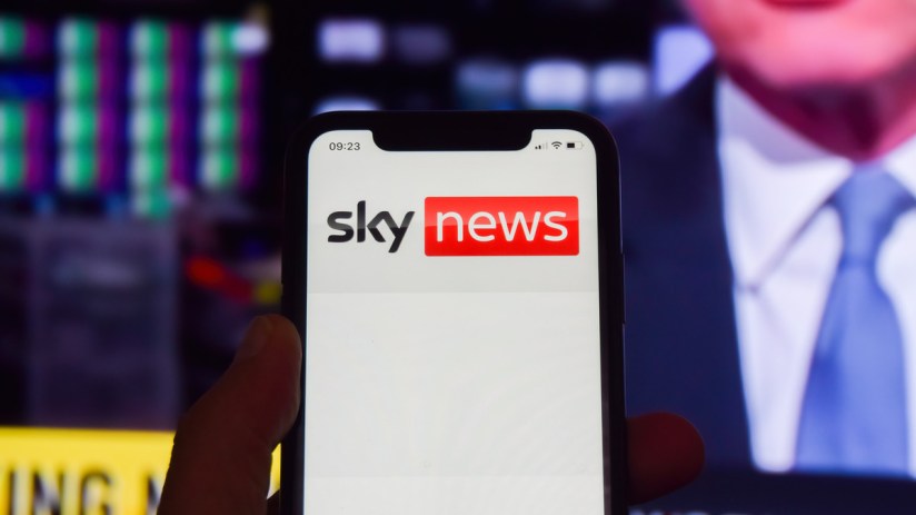 Sky News logo on a phone in front of a broadcast from the news channel