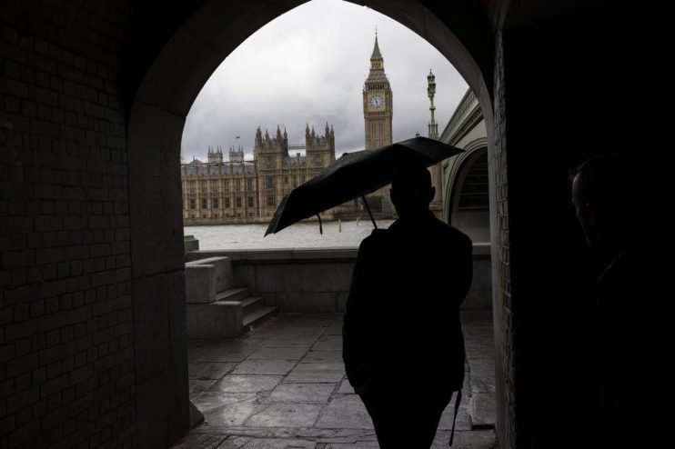 LONDON, ENGLAND - OCTOBER 21: A member of the public holds an umbrella opposite the Houses of Parliament on October 21, 2022 in London, England. Following Liz Truss's resignation as Conservative Party Leader and Prime Minister, candidates move to declare their intentions to run as her successor. (Photo by Dan Kitwood/Getty Images)