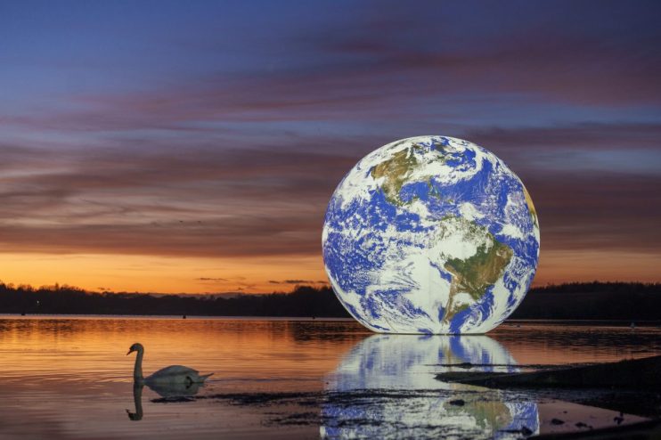 WIGAN, ENGLAND - NOVEMBER 22: The sun sets behind artist Luke Jerram's 'Floating Earth' at Pennington Flash on November 22, 2021 in Wigan, England. The floating Earth will hover over Pennington Flash for 10 days from November 19, as part of a celebration of Wigan and Leigh's watercourses and is the first time one of Jerram's globes has been floated on an open expanse of water. (Photo by Christopher Furlong/Getty Images)