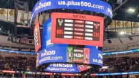 Plus500 branding on a large Jumbotron scoreboard at a US sports arena, displaying game stats.