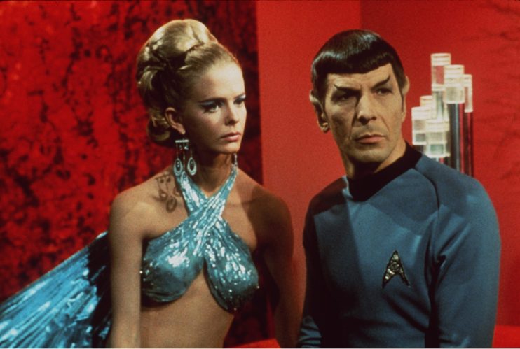 Spock from Star Trek in a classic pose with raised eyebrow, wearing a Starfleet uniform against a futuristic starship back...