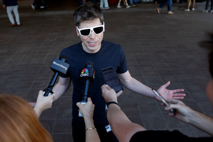Sam Altman discussing AI advancements at a tech conference podium, wearing a suit, with a large audience in the background.