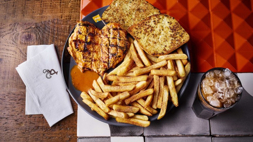 Nandos Chicken Butterfly with PERi-salted chips, garlic bread, and a bottomless Coke Zero on a restaurant table