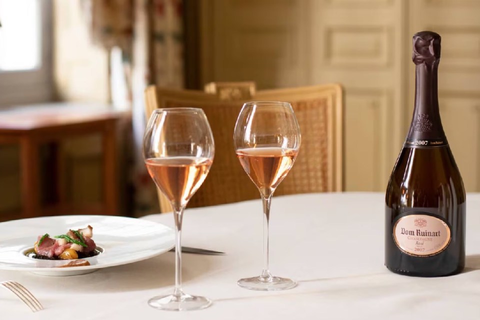 Ruinart champagne bottle with elegant label, surrounded by lush vineyard landscape, highlighting luxury and heritage.