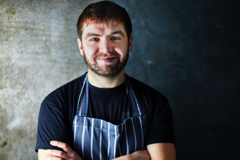Sebby Holmes cooking in a professional kitchen, showcasing culinary skills and expertise in a news feature on his career.