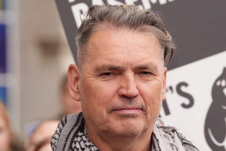 Labour donor Dale Vince smiling at a political event, wearing a suit and standing against a backdrop of party banners