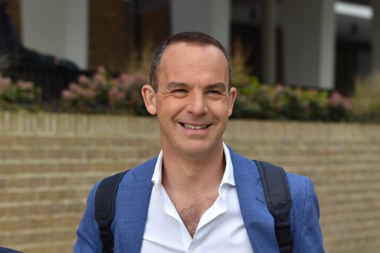Martin Lewis discussing financial advice on a news segment set, wearing a suit and gesturing with his hands.