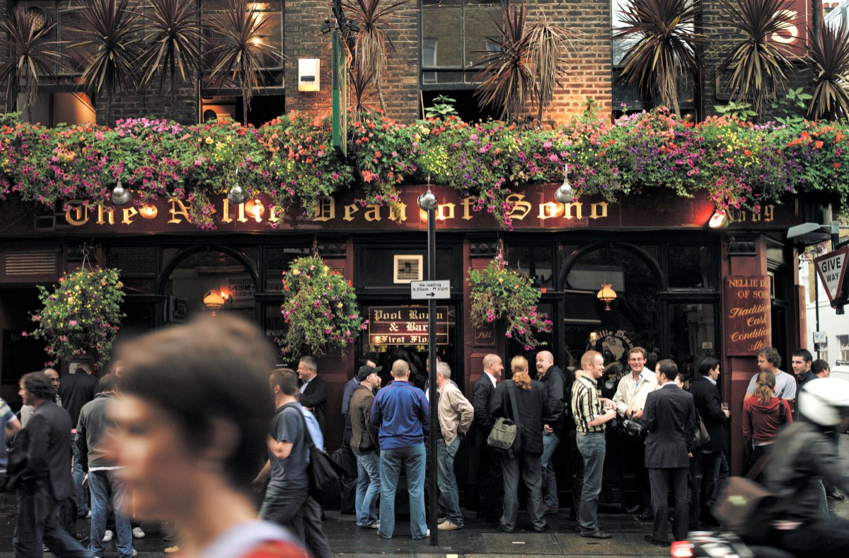 London pub exterior with historic architecture and patrons enjoying drinks on a sunny day, highlighting local social culture.