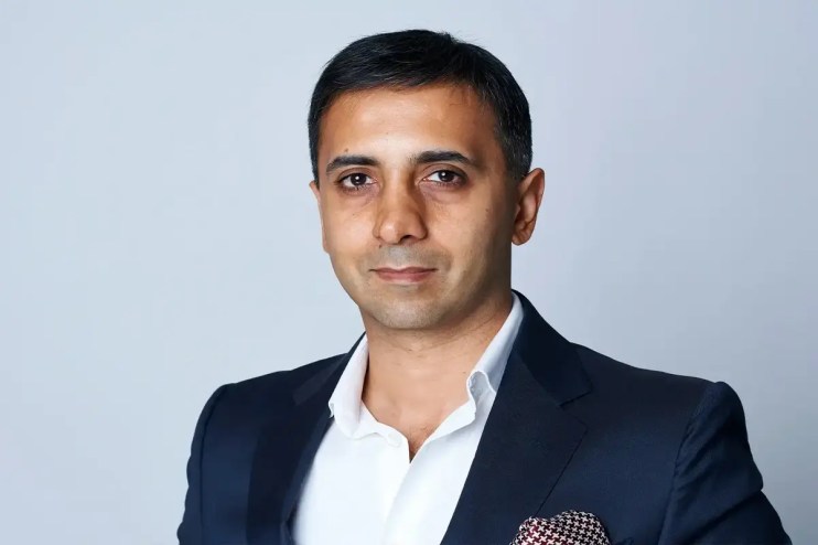 Tej Lalvani smiling during a business conference, wearing a suit and tie, highlighting his role as a prominent entrepreneur