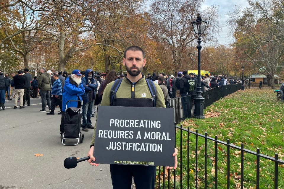 Antinatalist protestors gather with signs advocating against procreation in a city square, highlighting ethical concerns.