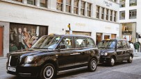 Black cab navigating Bond Street in Mayfair, showcasing Londons iconic taxi service against a backdrop of luxury shops.