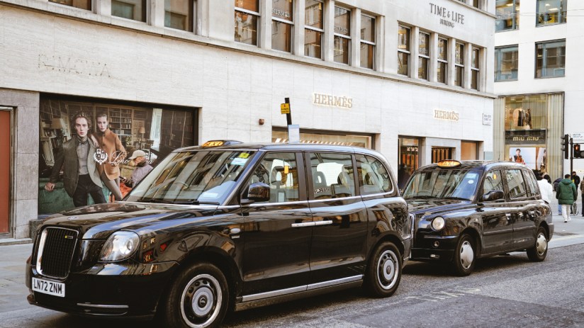 Black cab navigating Bond Street in Mayfair, showcasing Londons iconic taxi service against a backdrop of luxury shops.