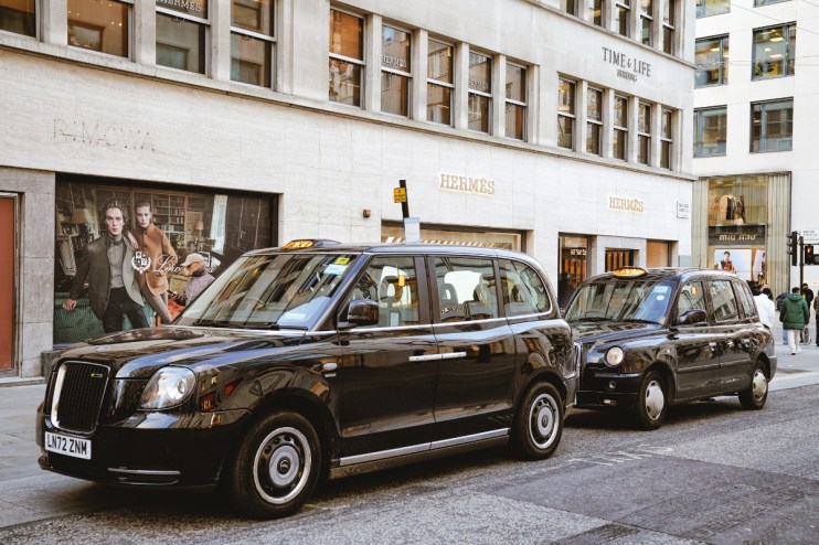 Black cab navigating Bond Street in Mayfair, showcasing Londons iconic taxi service against a backdrop of luxury shops.
