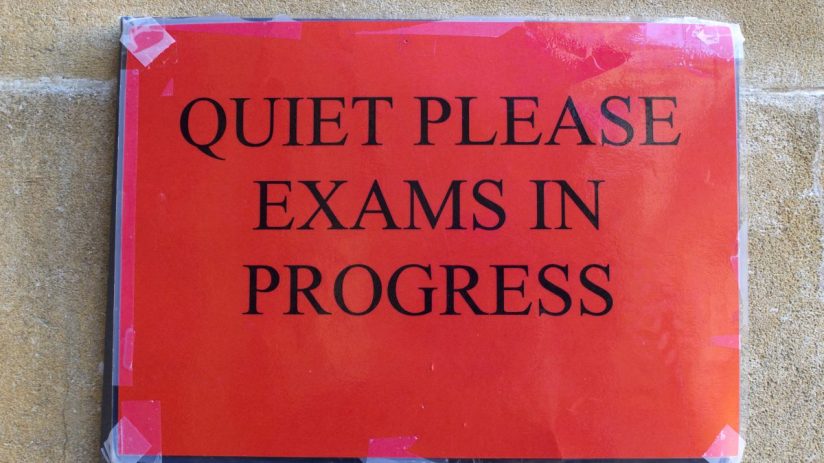 Students attentively taking in-person exams in a large classroom setting, showcasing a return to traditional test environm...