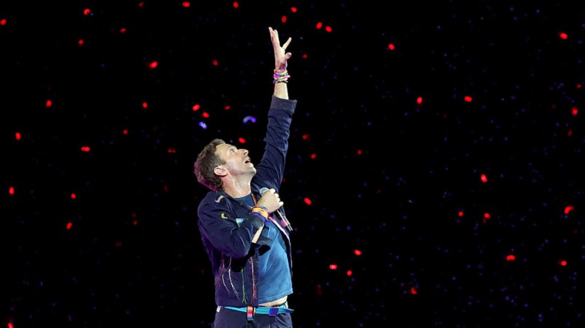 Coldplay band performing live on stage with vibrant lights and cheering crowd, showcasing their energy and musical talent.