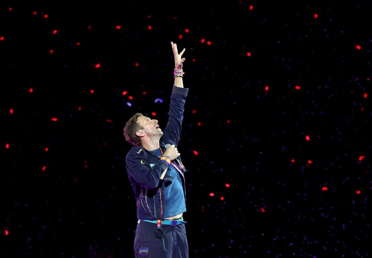 Coldplay band performing live on stage with vibrant lights and cheering crowd, showcasing their energy and musical talent.