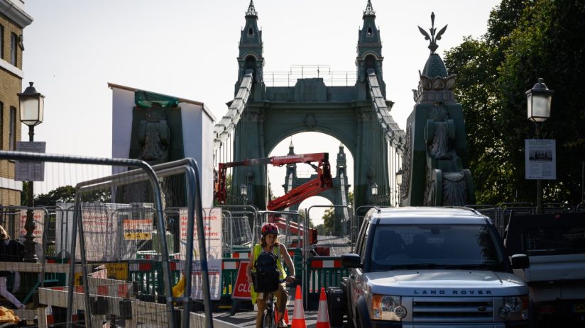 Hammersmith Bridge spanning the River Thames, surrounded by lush greenery and clear blue skies, capturing its iconic archi...