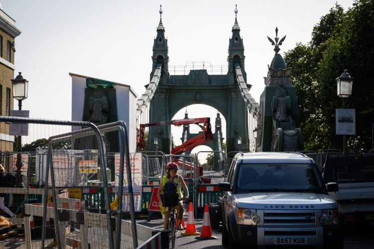Hammersmith Bridge spanning the River Thames, surrounded by lush greenery and clear blue skies, capturing its iconic archi...