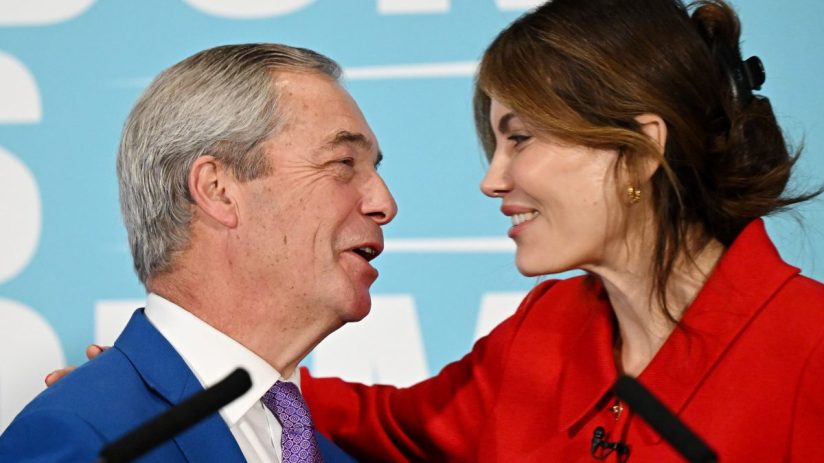Laila Cunningham and Nigel Farage discussing current events at a business conference podium, engaging audience attention.