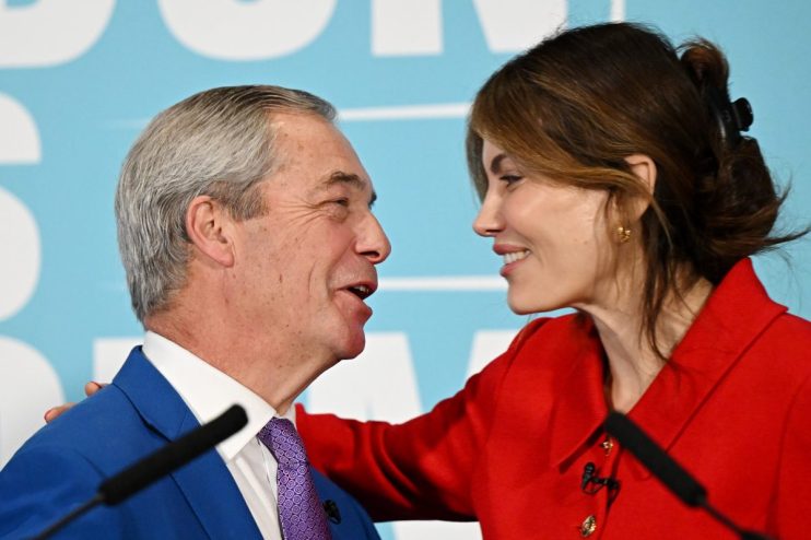 Laila Cunningham and Nigel Farage discussing current events at a business conference podium, engaging audience attention.
