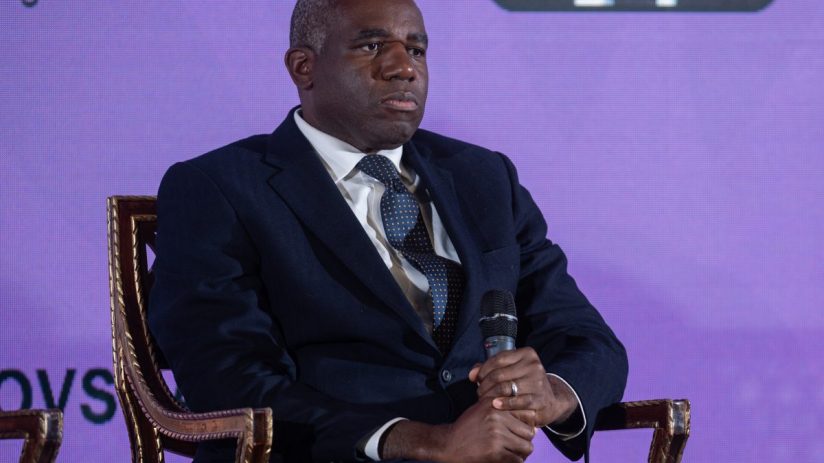 David Lammy speaking at a podium during a press conference, addressing current political issues, wearing a suit and tie.