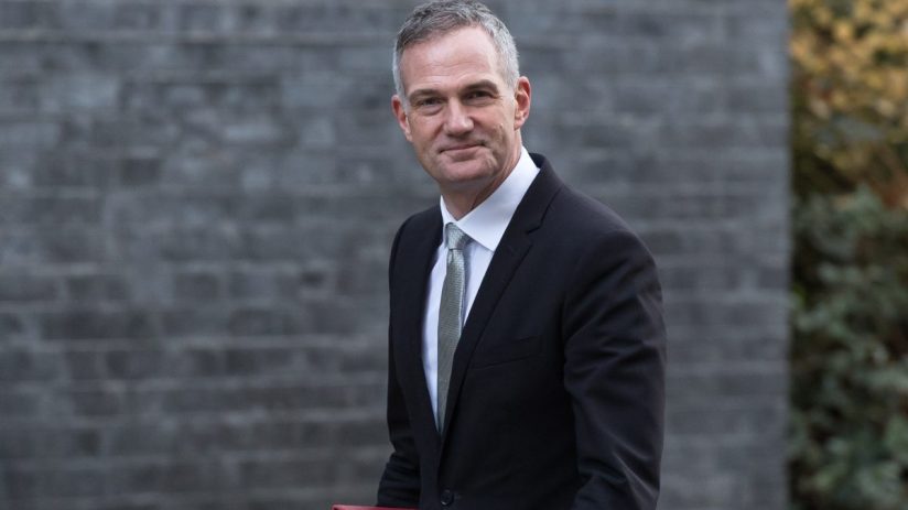 Peter Kyle addressing an audience at a business conference, wearing a suit and tie, with a presentation screen in the back...