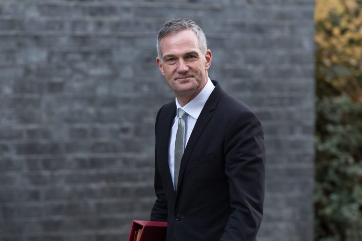 Peter Kyle addressing an audience at a business conference, wearing a suit and tie, with a presentation screen in the back...