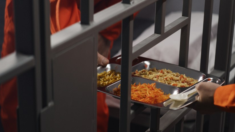 A tray of typical prison food with portions of mashed potatoes, green beans, and a meat patty, reflecting inmate meal stan...