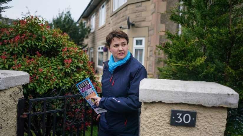 Ruth Davidson speaking at a public event, wearing a formal suit, addressing a large audience with a serious expression.