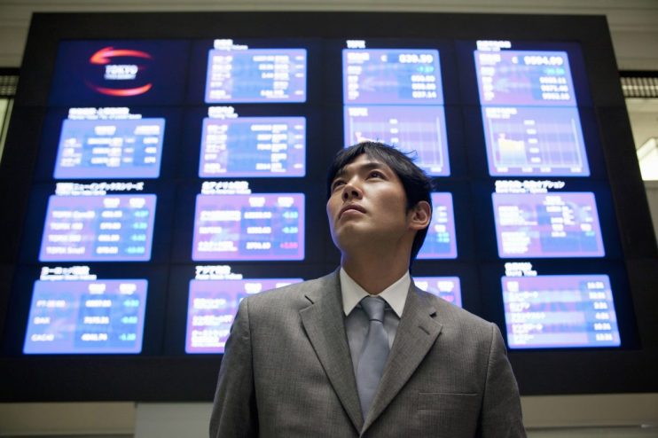Tokyo Stock Exchange trading floor with digital stock tickers displaying market trends and financial data.