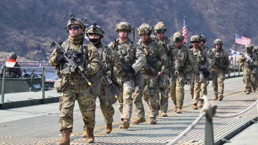US Army personnel in uniform engaged in strategic planning session in a conference room with maps and digital displays vis...