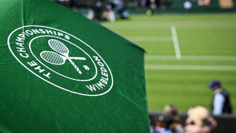 Wimbledon tennis match with players in action on grass court, surrounded by packed audience under clear skies
