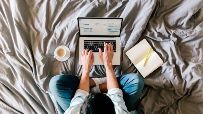 Person working remotely at a desk with a laptop, coffee mug, and notepad, representing modern work-from-home setup