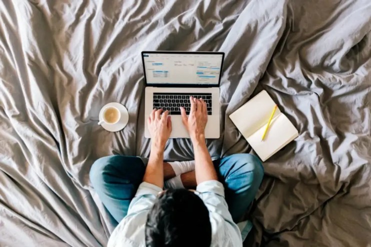 Person working remotely at a desk with a laptop, coffee mug, and notepad, representing modern work-from-home setup