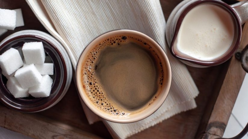 Freshly brewed coffee with a splash of milk and sugar cubes on a wooden table, highlighting morning beverage essentials