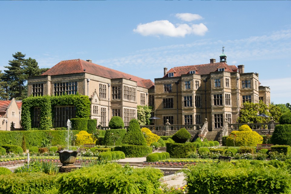 Fanhams Hall Hotels elegant garden with manicured lawns and colorful flower beds under a clear blue sky