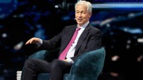 Jamie Dimon speaking at a JP Morgan event, wearing a suit and tie, addressing financial trends and market strategies.