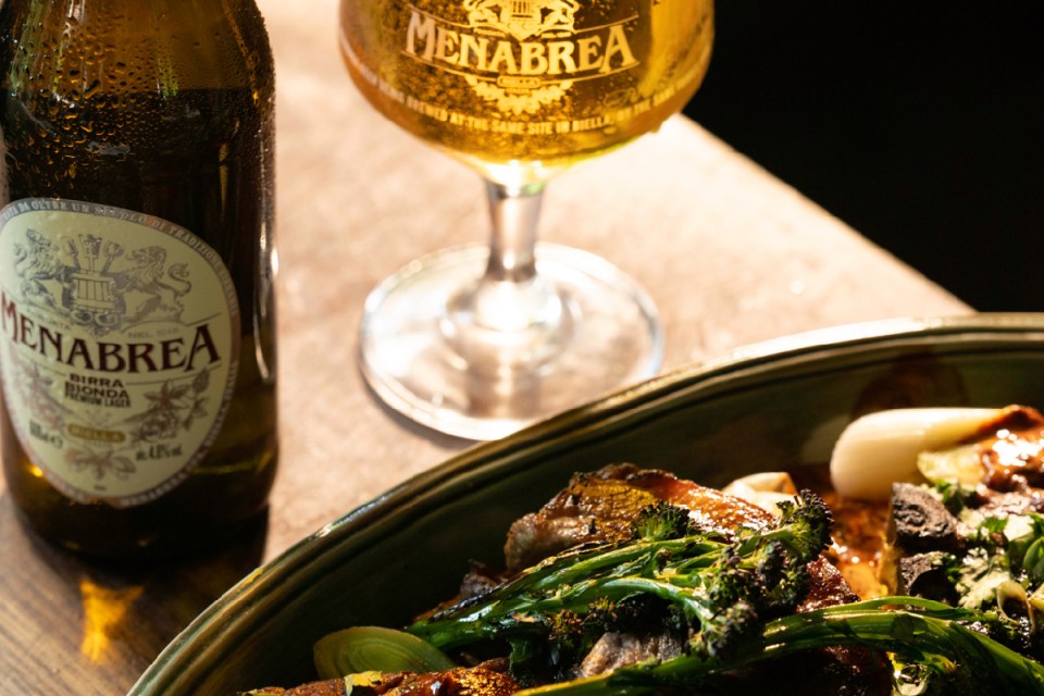 Menabrea beer bottles displayed on a wooden table, showcasing the brands label and amber color in a cozy pub setting.
